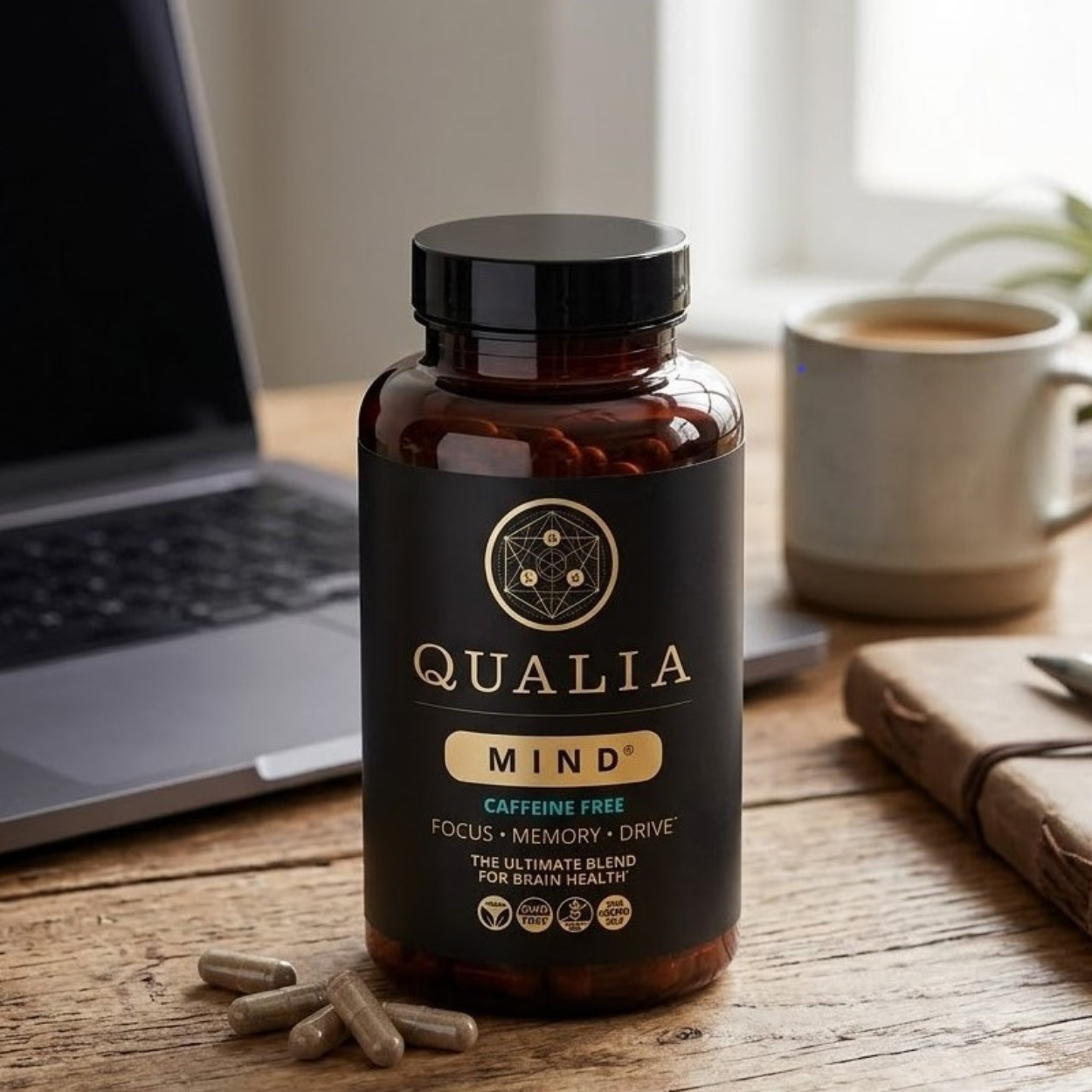 Qualia Mind Caffeine Free bottle on a wooden desk with laptop and coffee.